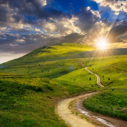 summer landscape. mountain path through the field turns uphill to the sky at sunset