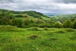 carpathian countryside landscape in spring. grassy meadows, rural fields and forested slopes on hills rolling off in to the distant village in the valley. overcast weather with clouds above the ridge
