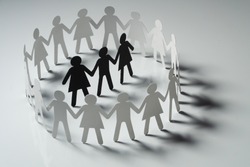 Three human paper figures surrounded by circle of paper people holding hands on white surface. Bulling, conflict, segregation concept.