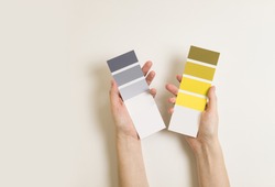 Women's hands hold swatches of the trendy colors - illuminating yellow and ultimate grey. Selection of year 2021 colors for design of clothes, interiors, websites and publications. Flat lay. 