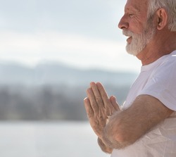 Portrait of senior man holding namaste pose and meditating outdoor beside river