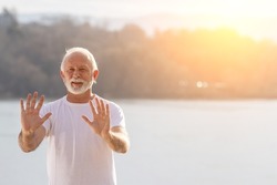 Portrait of senior man practicing tai chi chuan outdoor at sunset on river coast
