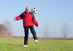 Old man in seventies kicking a soccer ball on playground