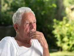 Portrait of old thoughtful man in park with green background. Senior care and depression concept