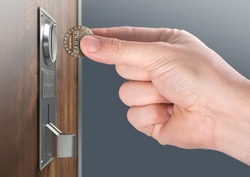 A male hand ready to insert a token into the slot of a vintage chrome coin receptacle mounted on a wooden surface - 3D render