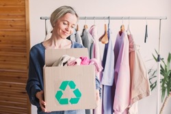 Woman selecting clothes from her wardrobe for recycle shop. Woman Decluttering Clothes, Sorting, And Cleaning Up. Reuse, second-hand. Conscious consumer, sustainability.