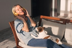 Peaceful middle aged female in modern headphones sit relax on comfortable couch listening to music, happy calm adult woman in earphones rest on cozy sofa, enjoy good quality sound, stress free concept