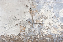 Extremely weathered facade wall.  few layers of paint peeling of the wall, showing cracked brown coating stucco. Cracks, missing patches of paint and blisters on the surface of paint.