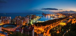 Malaga, Spain. Aerial view of City Hall? port and Bullring arena with illuminated buildings and Mediterranean sea in Malaga, Andalusia, Spain at night with sunset sky