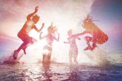 summer silhouettes of happy young people jumping in sea on the beach. vintage retro style with soft focus and sun flare