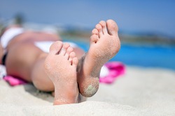 Woman's feet on the white sand near the sea.