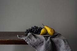 Still life with fruits. Grapes and pears on a rustic table indoors with a moody window light