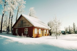 Snowy hills in Russian countryside in morning, red wooden house windows turned to east