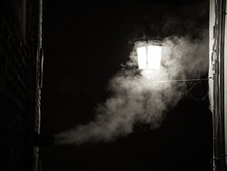 The smoke from a fireplace merges with the light of a street lamp during the night