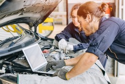 Meachnic staff worker using laptop computer check ane tuning car engine in garage