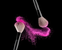 Make-up brush with pink powder explosion on black background
