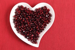 Red pomegranate seeds on a white heart-shaped plate.