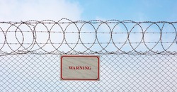 Warning sign hangs on a metal barbed wire fence ensuring safety and security. 
