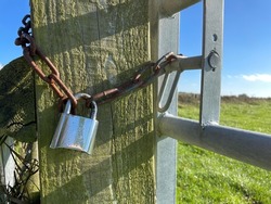 A farmyard gate is secured with a silver padlock and rusting chain around a heavy duty wooden post