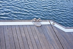 A folded spiral mooring rope with a end knot around a cleat on a wooden pier