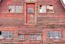 Old faded red wooden barn with broken windows, peeling paint and aged weathered wood.