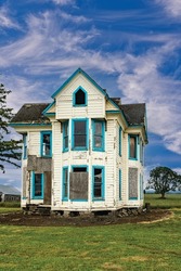 Old Wooden abandoned decaying white house and blue sky and clouds.