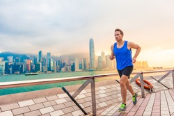 Running man runner in Hong Kong city urban skyline. Caucasian athlete training cardio jogging on the promenade of Victoria Harbor in HongKong, China, in afternoon sunset during summer.