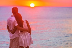 Couple in love watching sunset together on beach travel summer holidays. People silhouette from behing standing enjoying view of ocean on tropical destination vacation.