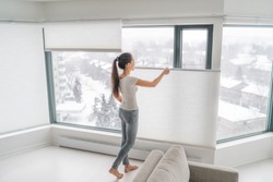 Woman opening home curtains in urban condo. Modern top down bottom up privacy cellular shades on apartment window keeping heat in winter with honeycomb blind curtain. Cordless pleated shades.