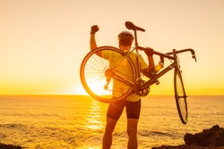 Success, achievement and winning concept with cyclist man road biking. Happy male professional athlete cycling raising arms lifting bike by sea during sunset cheering and celebrating at summit top.