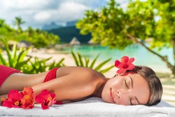 Woman relaxing at spa luxury massage hotel resort. Beauty girl lying down sleeping on towel with hibicus flowers outside. Serene ethnic woman relaxing. Mixed race Asian / Caucasian model outdoor.
