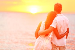 Honeymoon couple romantic in love at beach sunset. Newlywed happy young couple embracing enjoying ocean sunset during travel holidays vacation getaway. Interracial couple, Asian woman, Caucasian man.