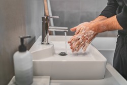 Washing hands with soap and hot water at home bathroom sink man cleansing hand hygiene for coronavirus outbreak prevention. Corona Virus pandemic protection by washing hands frequently.