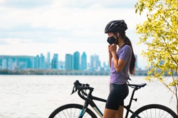 Wearing covid-19 mask while riding bike. Sport cyclist woman biking putting on face mask for Covid-19 prevention during summer outdoor leisure exercise activity. Fitness outside.
