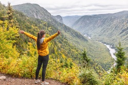 Happy woman hiking up mountain enjoying nature. Landscape with river view from top of trail hike. Girl with open arms outstretched in joy, enjoying travel fall in Jacques Cartier, Quebec, Canada. 