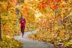 Autumn forest run path. Fall trail runner woman running in beautiful foliage woods nature background. Asian happy sports woman training outdoor. 