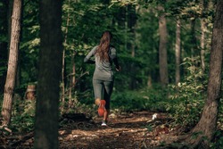 Exercising outdoors is healthy for active lifestyle runners. Autumn trail run woman running in nature from behind in dark forest. Outdoor jog.