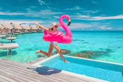 Luxury hotel beach vacation ocean overwater bungalows suite resort. Happy woman tourist jumping of joy in funny pool toy flamingo float excited to be in Bora Bora, French Polynesia.