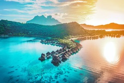 Luxury travel vacation aerial of overwater bungalows resort in coral reef lagoon ocean by beach. View from above at sunset of paradise getaway Bora Bora, French Polynesia, Tahiti, South Pacific Ocean