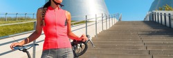 Road cycling in city cyclist athlete woman with bike wearing pink jersey outfit for sports biking on summer urban commute ride. Bicycle concept panoramic background.