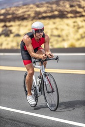 Triathlon time trial cycling triathlete man wearing aero bike helmet with visor biking on competition race day riding road bicycle vertical shot.