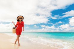 Luxury beach travel vacation elegant lady walking relaxing on holidays with beachwear accessories sunglasses, sun hat and bag wearing red cover-up dress.