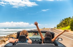 Road trip car holiday happy couple driving convertible car on summer travel Hawaii vacation. Woman with arms up having fun, young man driver