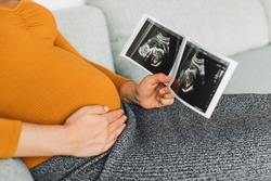 Pregnant woman looking at first ultrasound photo of her baby, caressing her belly happily awaiting the birth of her child. First trimester pregnancy