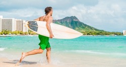 Hawaii surfing lifestyle young man sufer going to surf in blue ocean water in Honolulu, with Diamond Head in background. Oahu island travel vacation