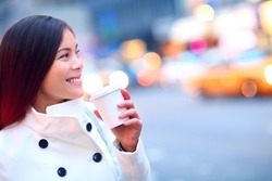 Professional young urban casual business woman in New York City Manhattan drinking coffee walking in street wearing coat downtown with yellow taxi cabs in background.