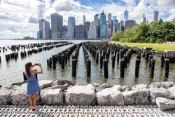 New York tourist woman taking mobile picture with smartphone. Manhattan city skyline waterfront lifestyle. People walking enjoying view of downtown from the Brooklyn bridge park Pier 1 salt marsh. 