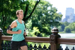 Man jogging in urban city NYC with smartphone armband. Male athlete runner running listening to music playlist on mobile phone app and earphones for workout run in New York's Central Park in summer.