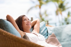Home lifestyle woman relaxing enjoying luxury sofa patio furniture on outdoor patio living room. Happy lady lying down on comfortable pillows daydreaming thinking. Beautiful young Asian chinese girl.