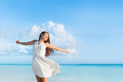 Freedom young woman with arms up outstretched to the sky with blue ocean landscape beach background copy space. Asian girl in white dress dancing carefree in sunset.
